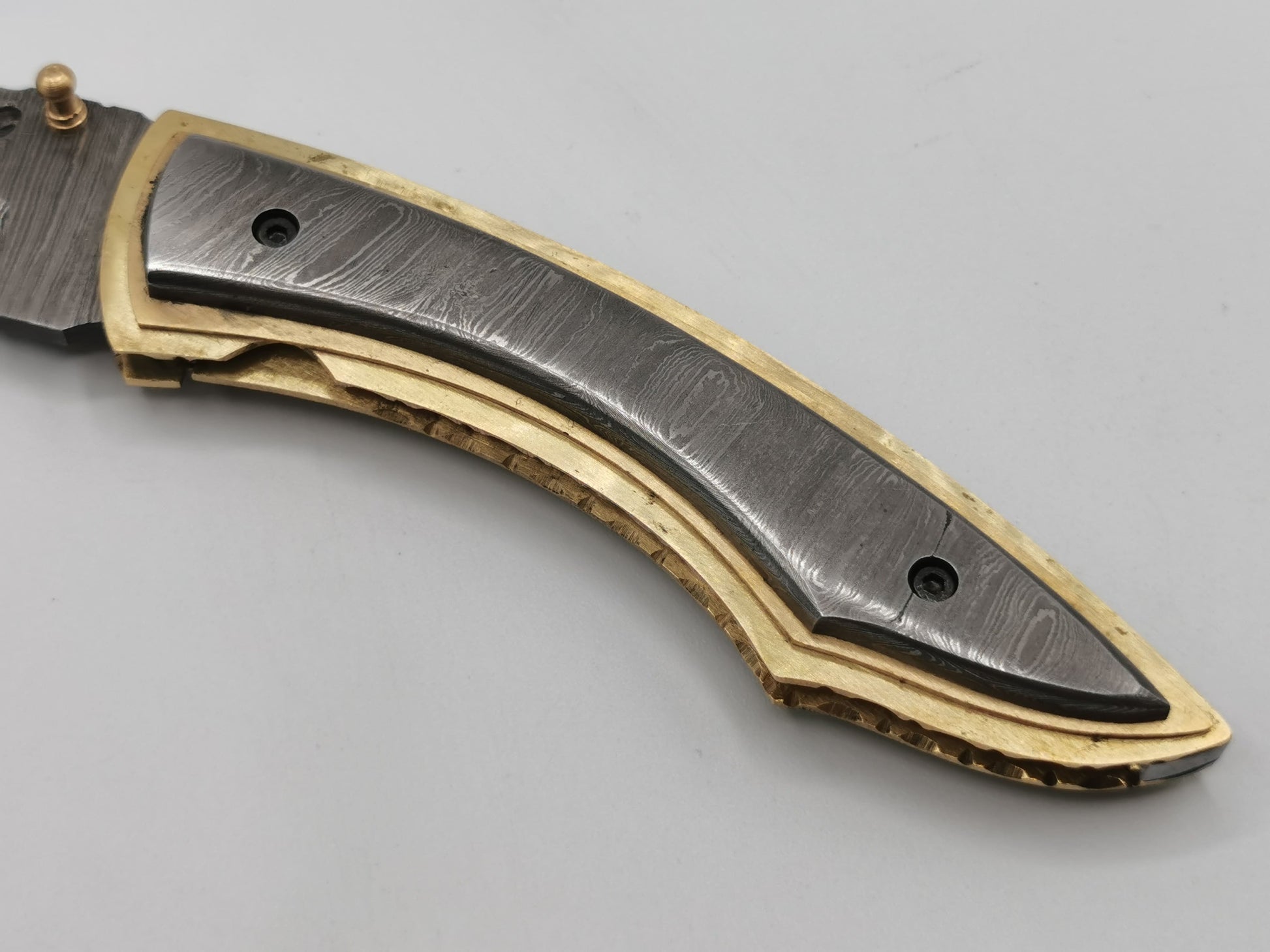 Détail du manche en acier damas et laiton massif du couteau pliant Le Olympe Hosteel