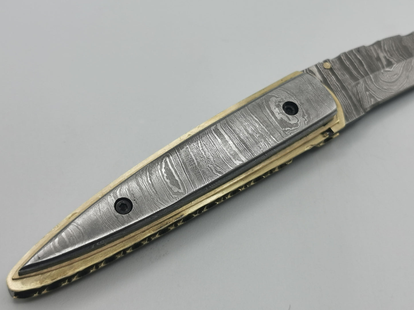 Gros plan sur l'extrémité pointue du manche acier damas et laiton, couteau Le Ferranel