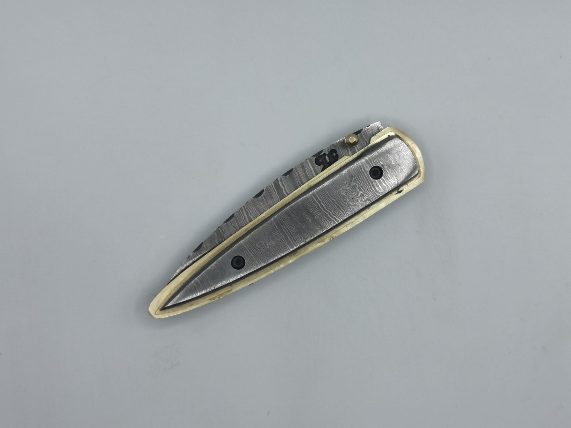 Détail du talon du manche en acier damas, finitions laiton du couteau Le Ferranel
