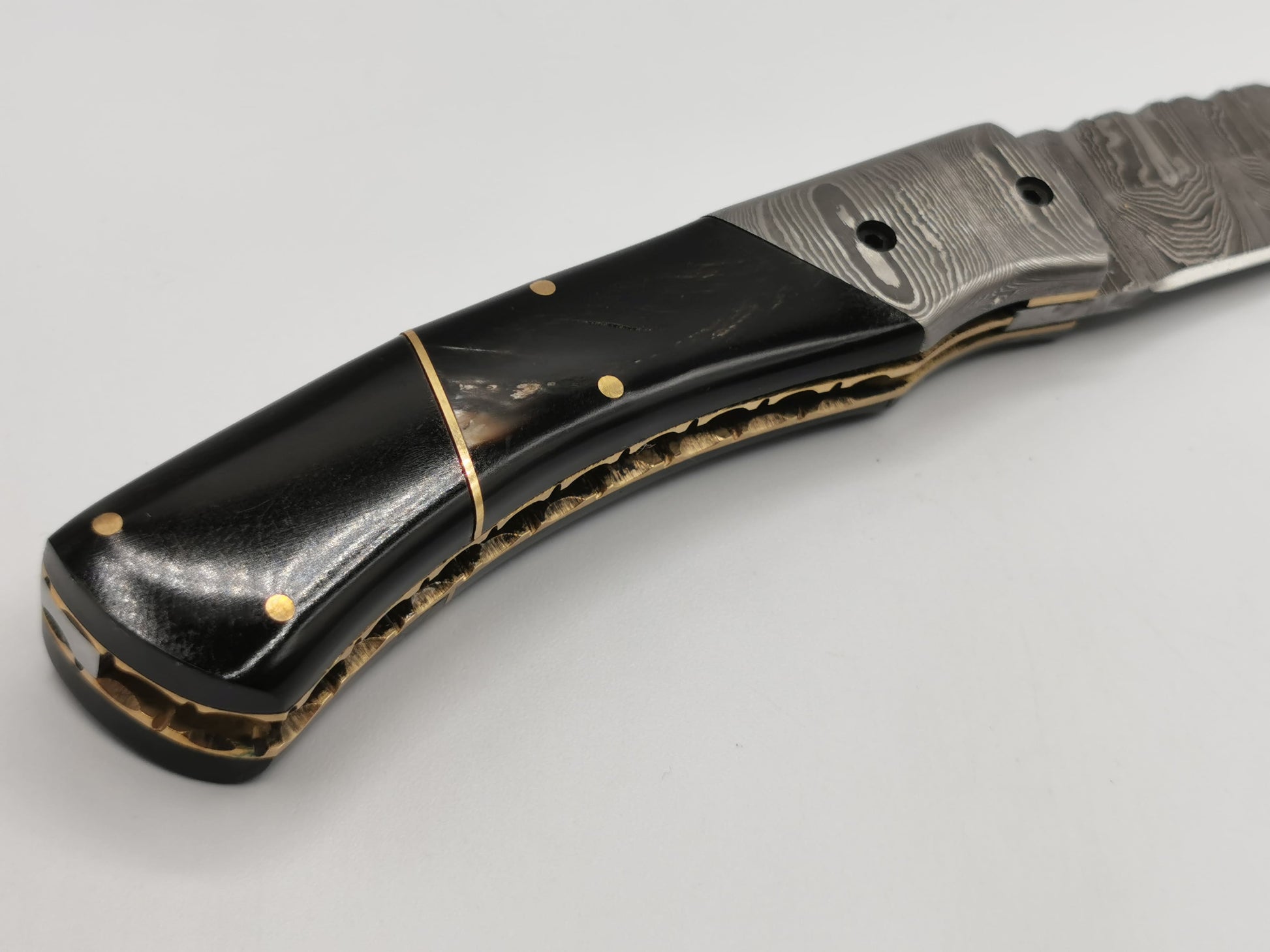 Détail du manche courbé du couteau Le Tramontane, alliant corne de buffle, acier damas et laiton